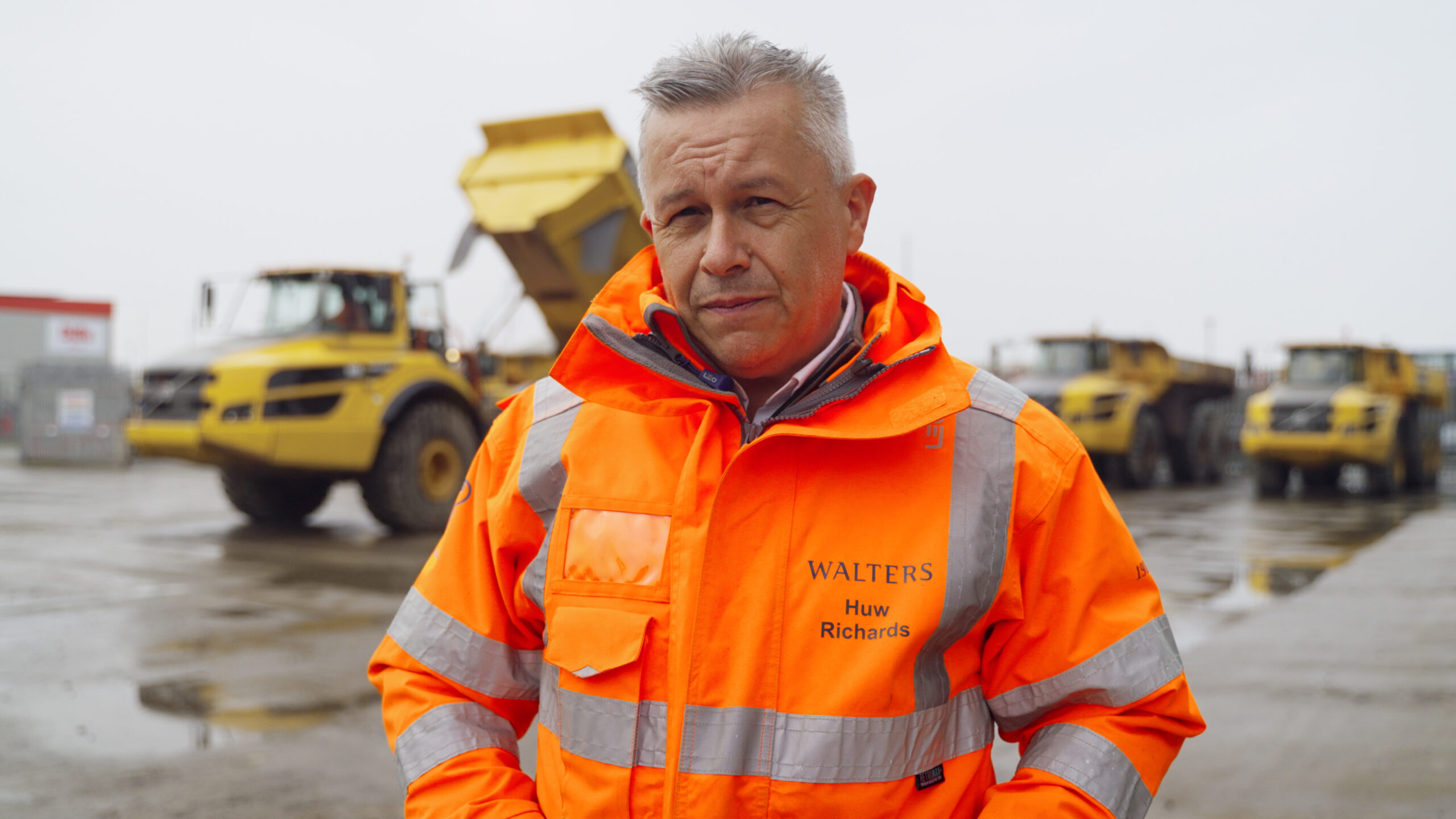 A man wearing a high-visibility jacket with the name "Walters" standing in front of the large heavy vehicle.